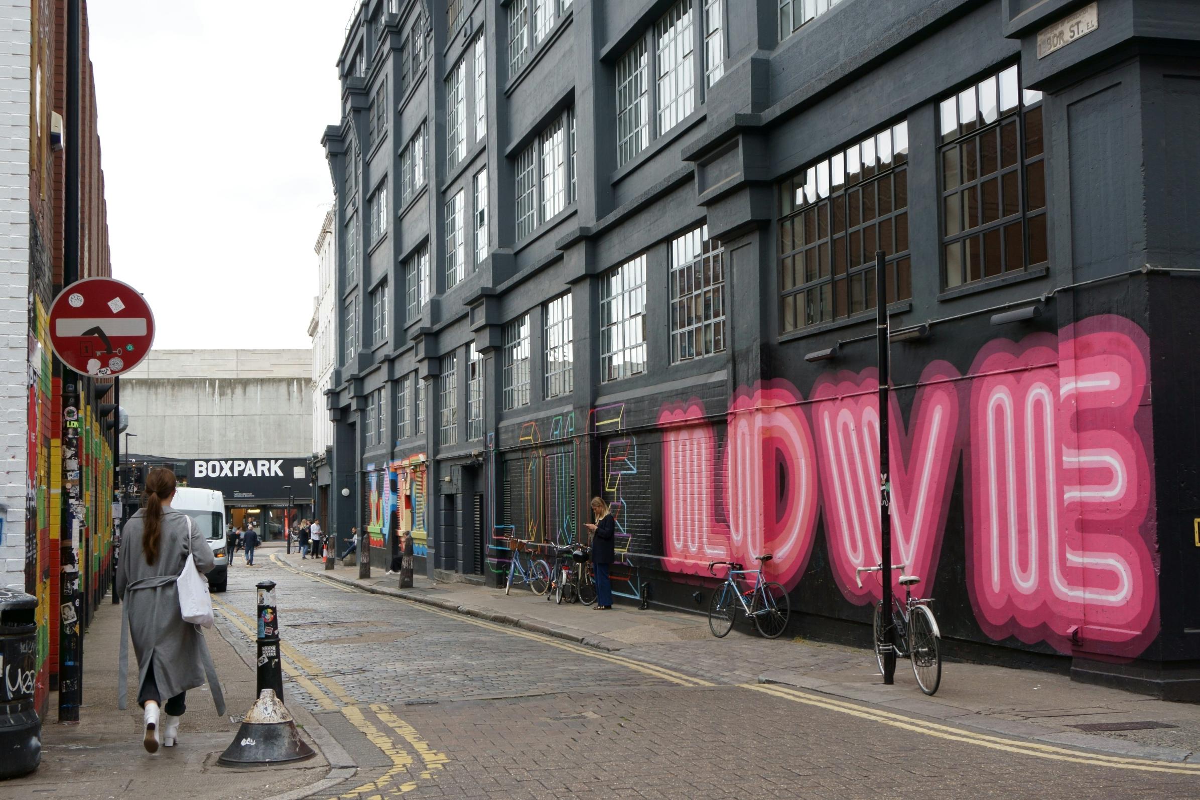 Woman walking down street with Love graphic on wall